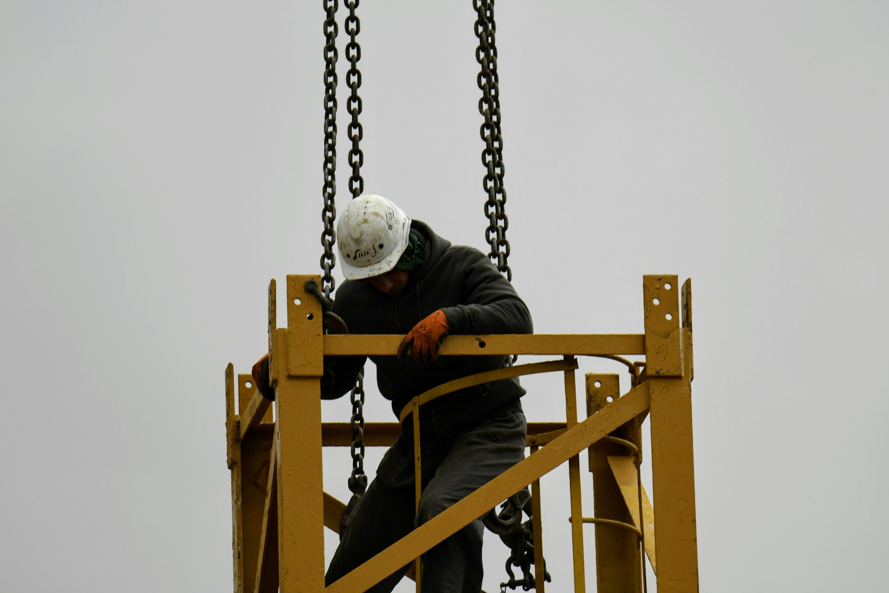 Construction worker working beside crane chains